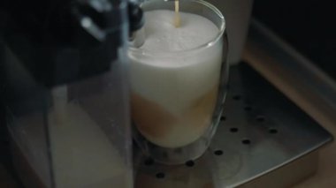 Modern coffee machine makes delicious cappuccino at home. Hot milk and boiled coffee poured into glass with white froth close view