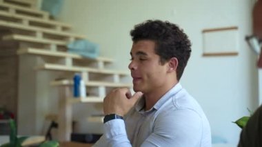 Colleagues sit at desk listening to mentor at teaching conference against stairs. Young brunet man enjoys learning new skills closeup slow motion