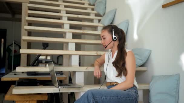 Woman Headset Participates Online Teaching Conference Laptop Sitting Wooden Stairs — Stockvideo