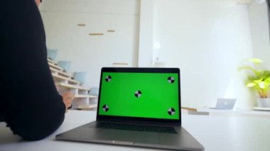 Man watches online teaching conference on modern laptop standing on white desk. Device with chromakey screen in office closeup place to insert
