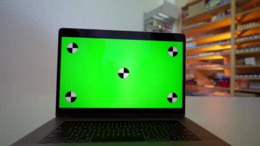 Man talks to manager via webcam using modern laptop standing on white desk in shop. Open gadget with green chromakey screen ready for tracking closeup