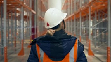 Blonde female engineer walks on aisle looking at empty racks due to shortage of goods. Woman in warehouse backside close view slow motion