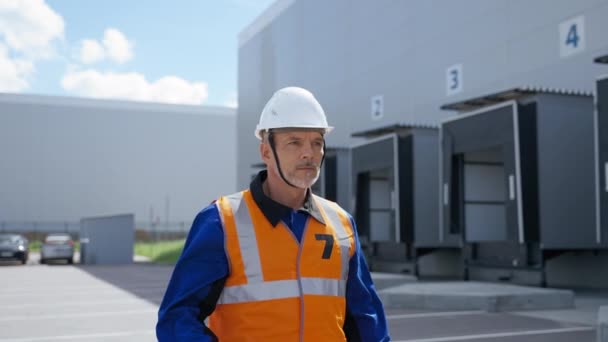 Bearded Engineer Walks Large Warehouse Adjusting White Helmet Sunny Day — ストック動画