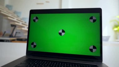 Man watches online courses on laptop with green chromakey screen. Modern electronic device stands on white table in office close view