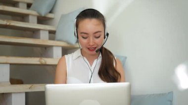Young woman in headset conducts online conference sharing useful knowledge. Female mentor uses laptop for communication sitting on stairs closeup