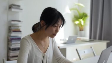 Delighted Asian woman types text for new project on laptop. Young female freelancer works online using modern gadget in home office closeup
