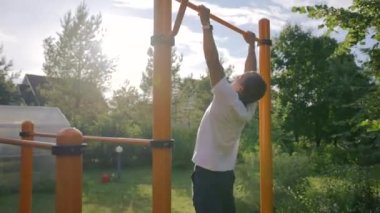 Middle-aged sportsman catches up and pulls on crossbar in own garden. Mature gymnast enjoys healthy lifestyle and tries to keep fit doing workouts in back lit