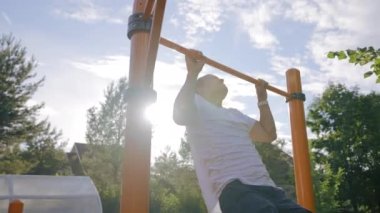 Middle-aged man puts effort catching up on crossbar in back lit. Mature man spends free time doing sports in cottage backyard. Adult enjoys healthy lifestyle