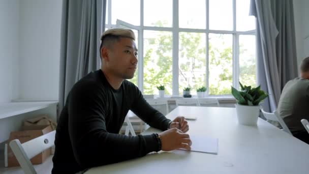 Asian Blond Dyed Man Sits Desk Large Bright Window Listening — Wideo stockowe