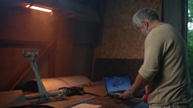 Aged man makes measurements of future plane. Senior makes plane looking at digital model on laptop. Man assembles own aircraft according to drawings
