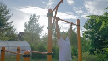 Mature man enjoys healthy lifestyle doing tricks on pull-up bar. Middle-aged person shows strength and power doing tricks in own cottage house backyard