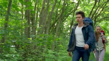 Couple of young tourists hikes in dense forest. Young girlfriend stops and asks for help. Brown-haired lady looks with tired and exhausted expression