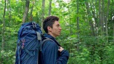 Black-haired young man discovers awesome forest destination standing. Guy camper enjoys hiking in forest. Sunlight breaks through tree branches closeup
