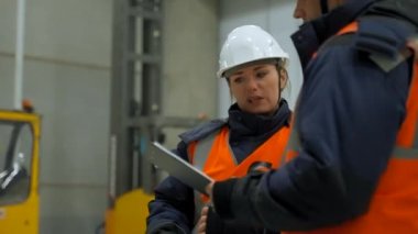 Engineers in white helmets look at clipboard discussing plan of work. Woman and man stand in storage terminal talking closeup slow motion