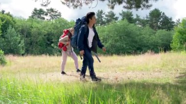 Young couple of hikers stops near big tree to hide from rain on glade. Man and woman find perfect spot for camping in forest putting bright backpacks on grass