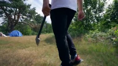 Bully runs with sharp axe to young couple near camp tent threatening people. Young man stands up and runs quickly to safe girlfriend. Couple tries to survive
