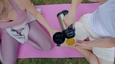Boyfriend pours tea from thermos into mugs. Couple enjoys drinking tea together sitting on pink mat. Young people spends weekends in fresh air