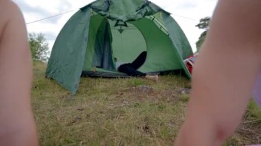 Young couple watches together interesting film via laptop sitting on pink mat. Black-haired man explains scenes to girlfriend waving hands against camp tent