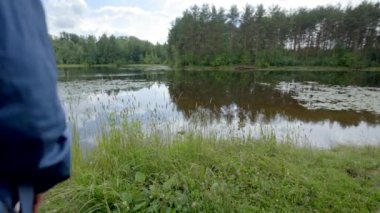 Couple of young hikers stands looking at calm overgrown forest lake. Girlfriend and boyfriend wearing casual clothes enjoy picturesque landscape