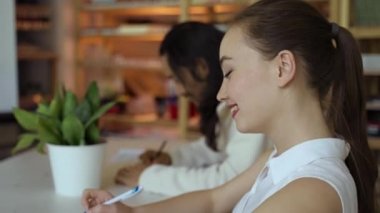 Young woman and man sit at desk in office developing new project. Colleagues write plan of work with pen on paper sheet by pot-plant closeup slow motion