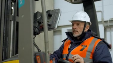 Bearded engineer sits in forklift cabin pushing button on monitor. Man in uniform checks condition of equipment in storehouse closeup slow motion