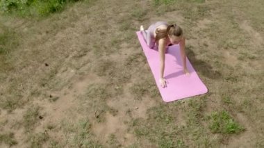 Young woman does yoga asana raising both hands above head. Sporty lady in pink sports suit practices pose uniting with nature against high green trees upper view