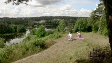 Young man and woman practice yoga Camel pose on mats on steep river bank together. People concentrate on asana enjoying moments on high hill