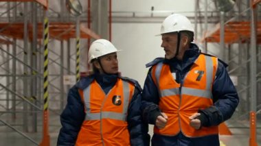Concerned man and woman discuss global economic crisis walking on aisle between empty metal racks. Engineers in uniform at work in warehouse slow motion