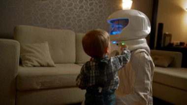 Bir çocuk babasının dairesinde astronotların takım elbisesinin düğmelerine basar. Geceleri rahat bir evde bir çocukla oynamak için fütüristik bir kostüm..