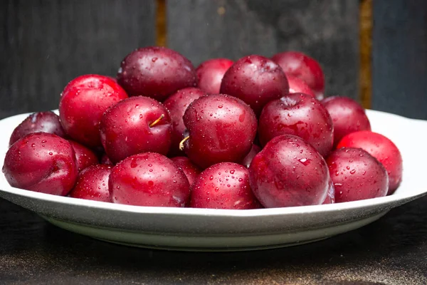 Fruits frais de prune rubis sur une assiette blanche, servis sur une table en bois. — Photo