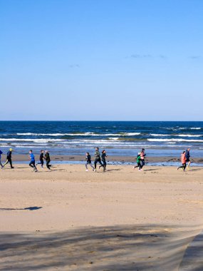 Bir grup insan deniz kenarında bir maraton koşuyor.