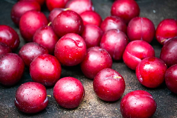 Burgundy plums are scattered on the table in droplets of water. — Stock Photo, Image