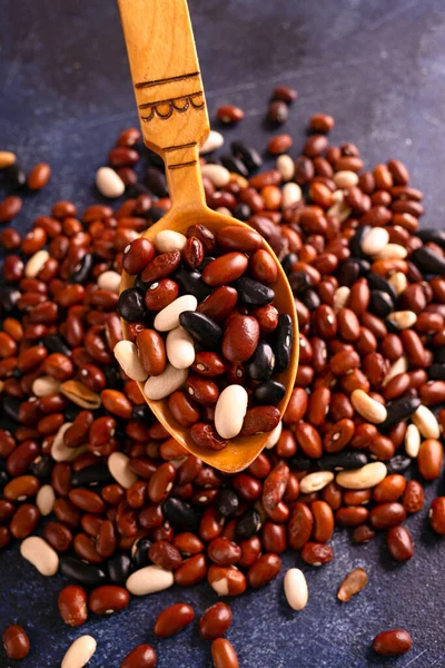 Red, black, white beans in a wooden spoon on a rustic table