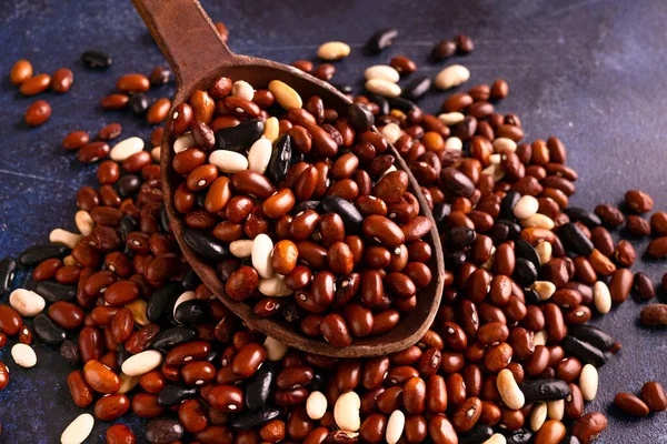 Red, black, white beans in a wooden spoon on a rustic table.