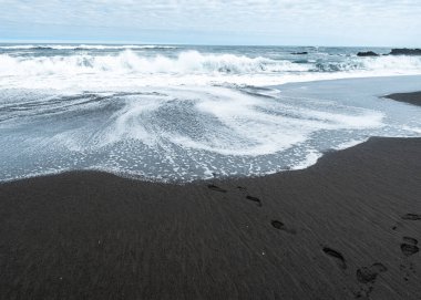 Pikhilemu 'nun siyah kumunda denize bakan insan ayak izleri.
