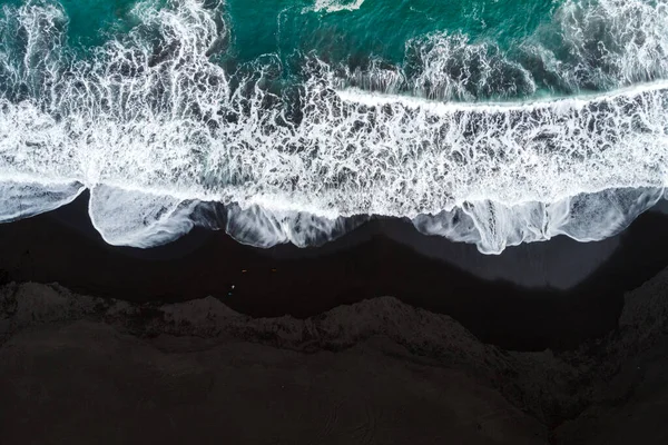 Siyah kumlu bir sahil manzarası ve denizin mavi suları..