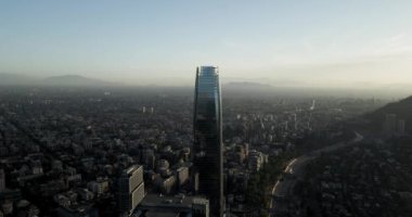 Santiago şehrinin hava yörüngesinde binaları ve dağları gün batımında arka planda..