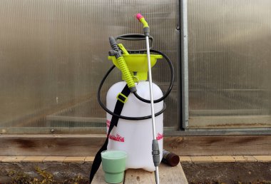 Kapalı bir seranın arka planına pompa püskürtücü ve plastik bir bardakta Bordeaux sıvısı çözeltisi