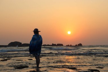 Okyanusta gün batımında yalnız bir kadın figürü. Yalnızlık ve bekleyiş