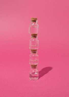 Cam şişeler pastel pembe arka planda dizilmiş.