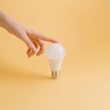 Sarı arka planda bir kadının eli ampulü tutuyor. Fikir, ışık, yaratıcılık.