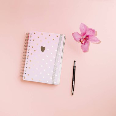 Pembe arkaplanda pembe bir orkide ve kurşun kalemle duran kalplerle dolu bir defter. Notlar, düşünceler, planlar ...