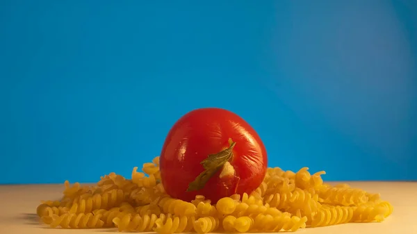 macaroni macaroni close-up isolated on blue and tomato on top