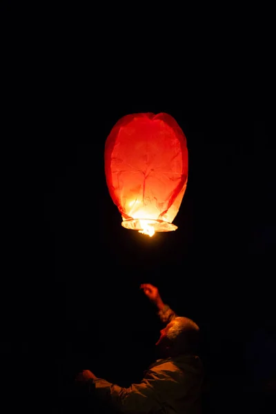 Homem idoso adulto com cabelos grisalhos lançando lanterna de papel laranja com fogo ardente no céu na noite escura Imagem De Stock