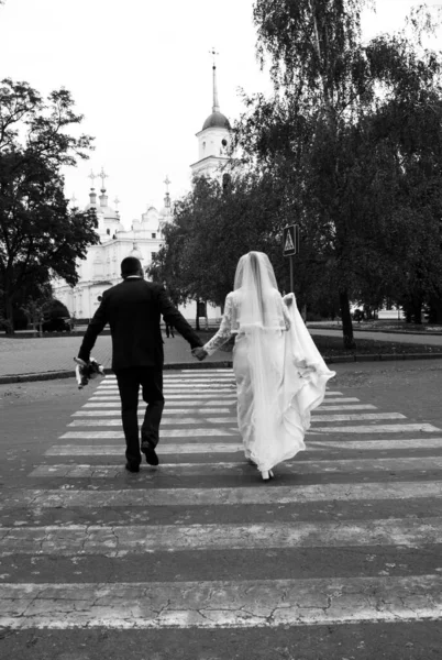 A noiva e o noivo em um pedestre que cruza na cidade das costas. Casamento casal cruzando a estrada foto preto e branco — Fotografia de Stock