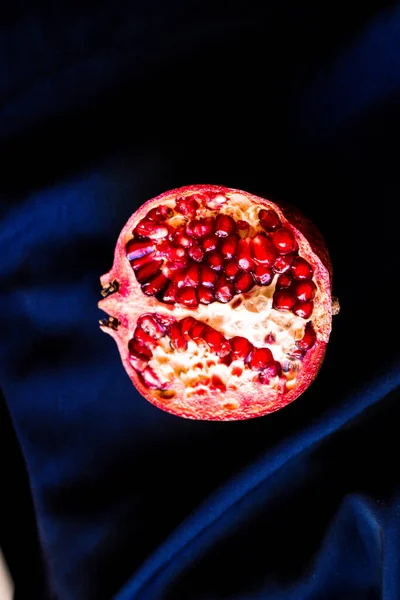 Half a pomegranate on a dark fabric background. Deep red saturated pomegranate fruit on black and blue silk fabric — Stock Photo, Image