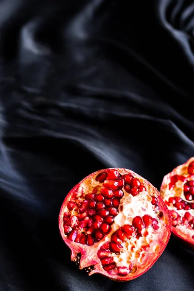 Ripe juicy pomegranate halves on silk fabric. Deep red saturated pomegranate fruit on black silk — Stock Photo, Image