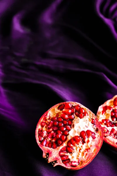 Ripe juicy pomegranate halves on silk fabric. Intense red pomegranate fruit on purple silk — Stock Photo, Image