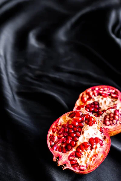 Two halves of a pomegranate on a silk fabric. Dark red rich ripe pomegranate fruit on black silk — Stock Photo, Image