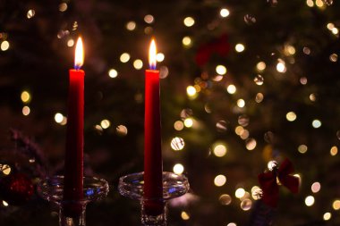 Uzun cam şamdanlarda iki uzun kırmızı mum Yeni Yıl ağacının arka planında. Romantik bir ortamda mum ışığında bir kutlama. Arkaplanda Bokeh etkisi